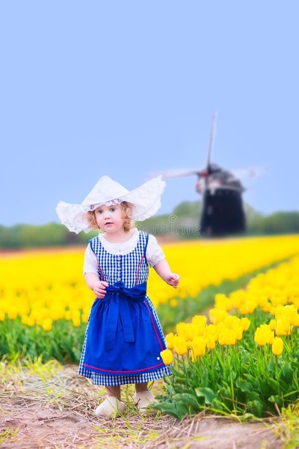 Pretty girl in Dutch costume in tulips field with windmill