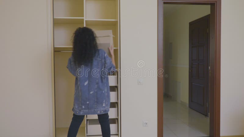 Pretty girl put a box with things in an empty wardrobe in a new house