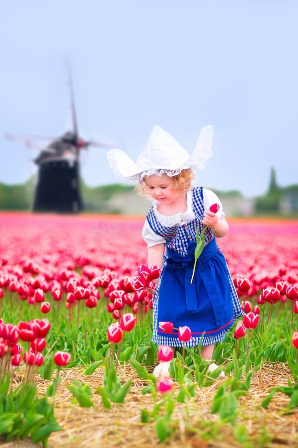 Pretty girl in tulips field with windmill in Dutch costume
