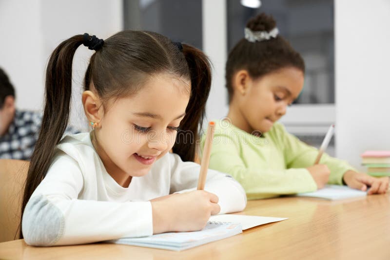Pretty girls sitting at desk in class, writing in copybook. stock photo Pretty girls sitting at desk in class, writing in copybook. stock photo