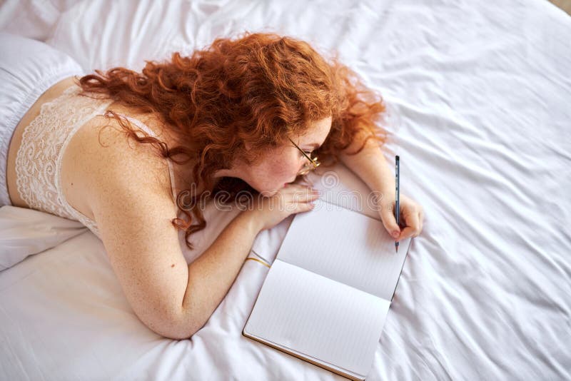 Pretty half-naked redhead woman make notes lying on bed