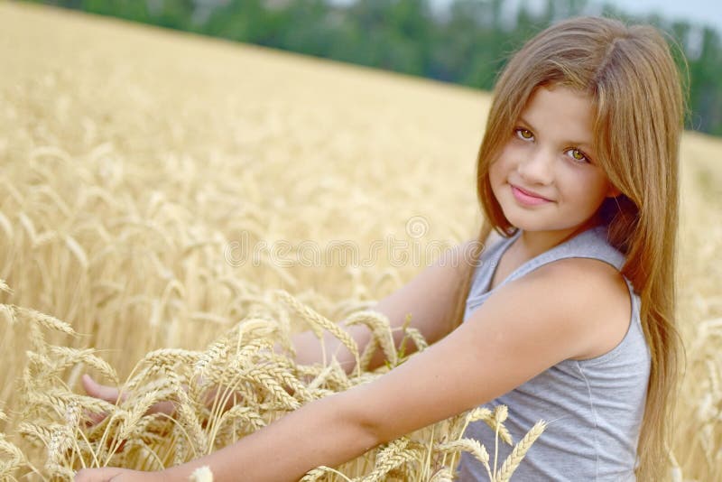 A pretty happy girl embracing by hands the golden rye ears in field. Concept of purity, growth, happiness