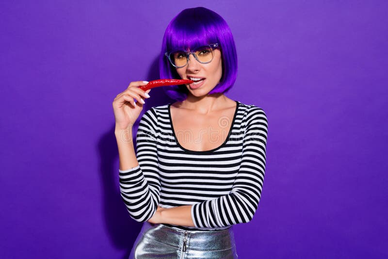 Pretty lady hold red chili pepper in mouth fearless person likes spicy food wear specs striped pullover isolated purple