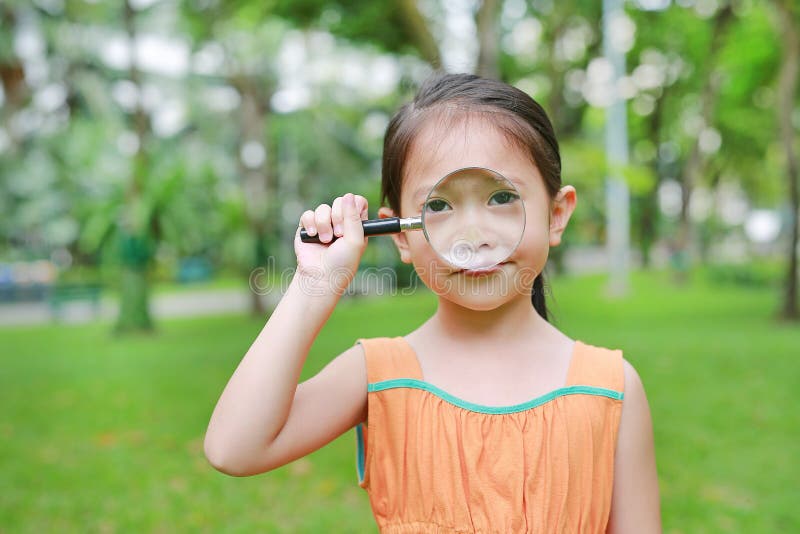Pretty little Asian child girl with magnifying glass looks at flower in summer park stock images Pretty little Asian child girl with magnifying glass looks at flower in summer park stock images