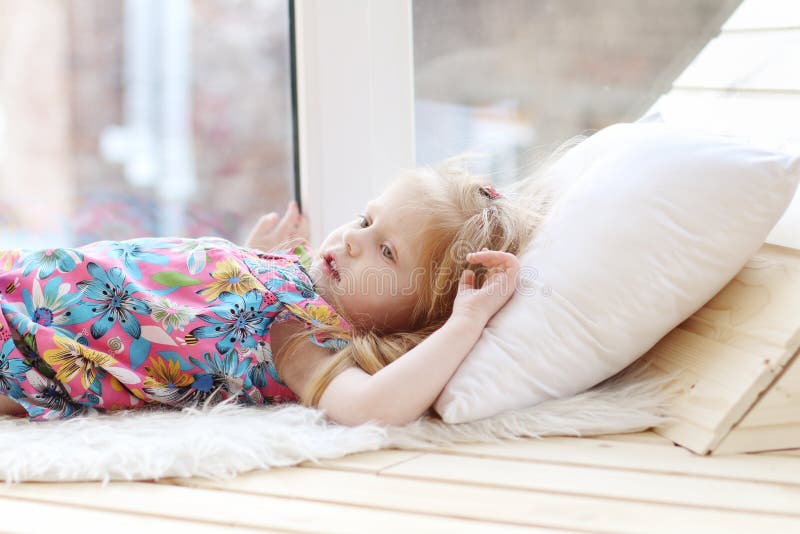 Pretty little blonde girl lies on white pillow near window