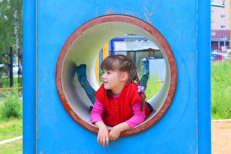 Pretty little girl lies in pipe on playground
