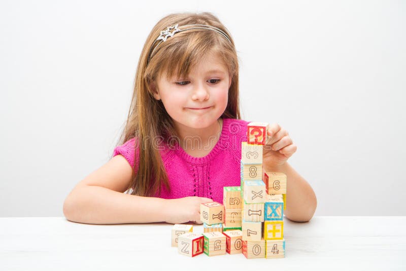 Pretty little girl playing with wooden cubes with letters and numbers royalty free stock photo