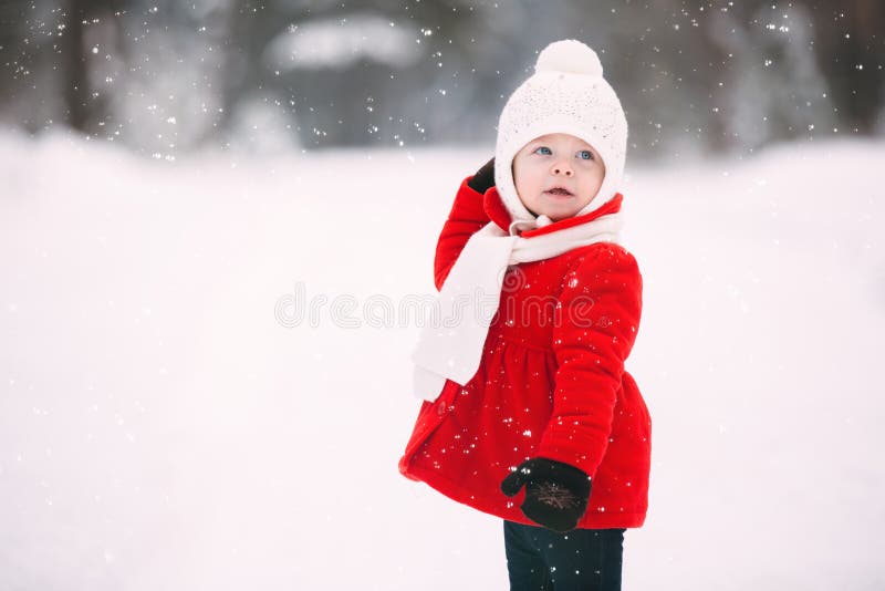 Pretty little girl in red coat in winter forest. cheerful little baby girl in gloves and white hat runs on snow white