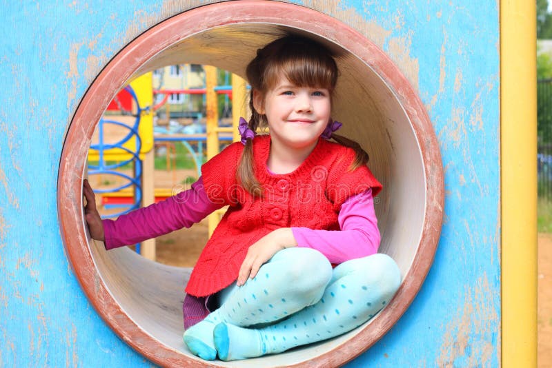 Pretty little girl sits in pipe on playground