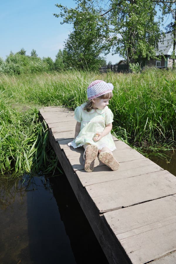 Pretty little girl sits on small bridge in village