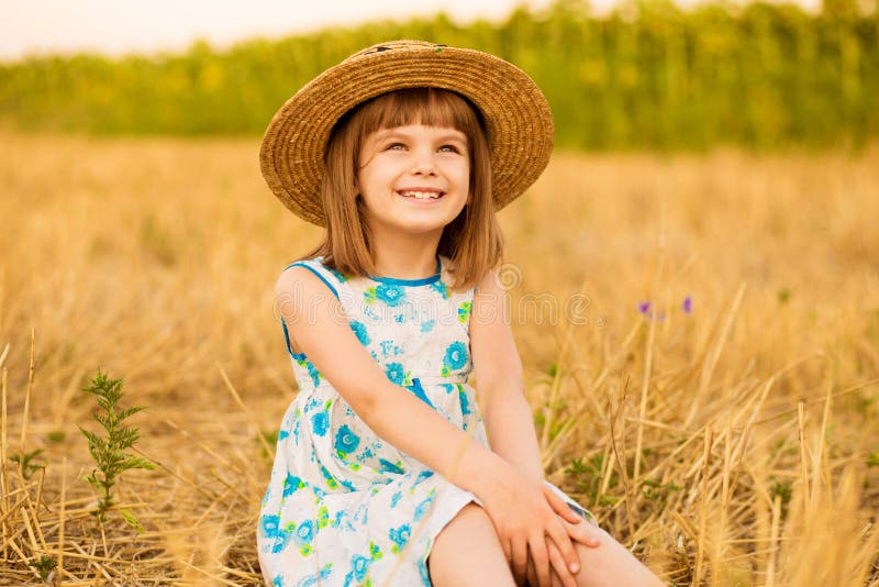 Pretty little girl in straw hat and dress walk in summer field. Sunny day