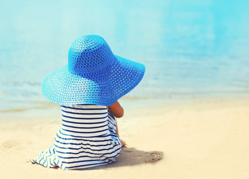 Pretty little girl in striped dress and straw hat enjoying sea