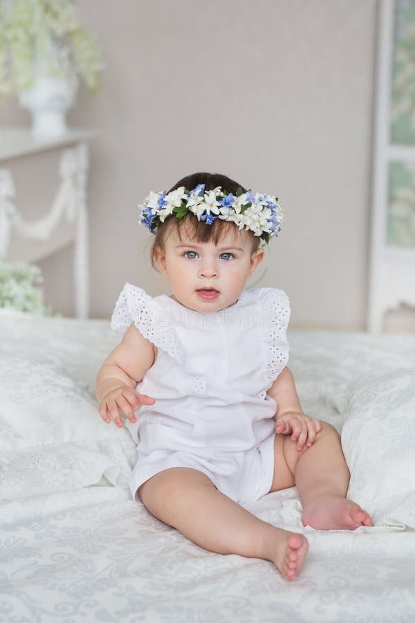 Pretty little girl in a white dress and with a diadem on a head sits on a bed stock photo Pretty little girl in a white dress and with a diadem on a head sits on a bed stock photo