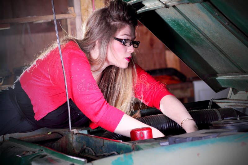 Una giovane e bella ragazza del college con lunghi capelli biondi dritti al lavoro su un veicolo, con entrambe le mani nel motore.