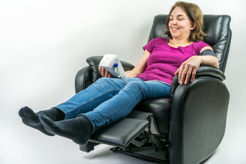 Pretty middle-age woman sitting in black leather recliner armchair. Checking blood pressure using portable blood pressure machine. stock photography Pretty middle-age woman sitting in black leather recliner armchair. Checking blood pressure using portable blood pressure machine. stock photography