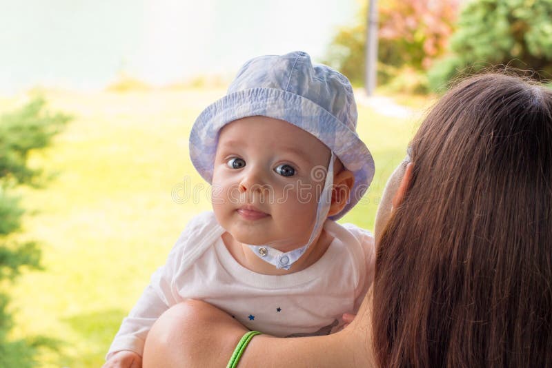 Innocent baby face portrait in sun hat above mother`s shoulder on nature bakcground stock images Innocent baby face portrait in sun hat above mother`s shoulder on nature bakcground stock images