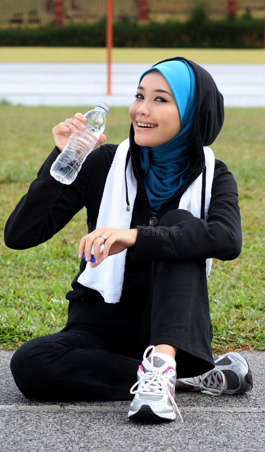 A pretty muslim woman athlete resting while drink