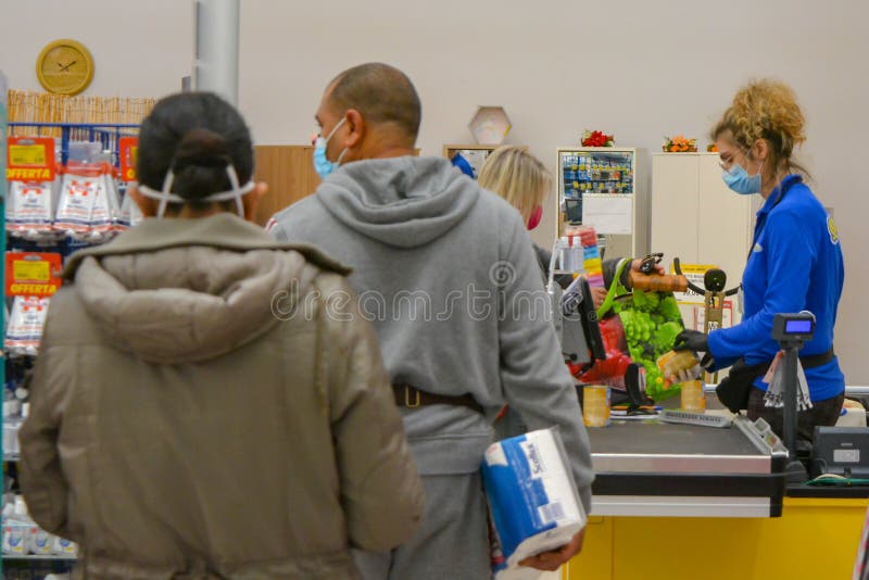 A pretty saleswoman at cash register wearing face mask. Customers buy toilet paper during pandemic