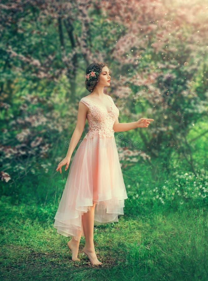 Pretty slender girl with braided dark hair with a barrette in a delicate elegant peach dress, a fairy-tale princess in a