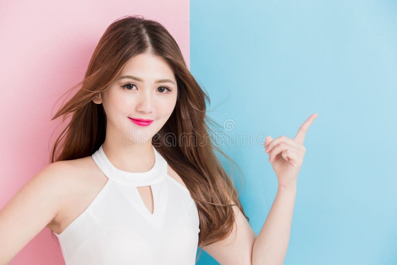A pretty smile girl standing with arms akimbo and pointing at pink and blue background. A pretty smile girl standing with arms akimbo and pointing at pink and blue background.