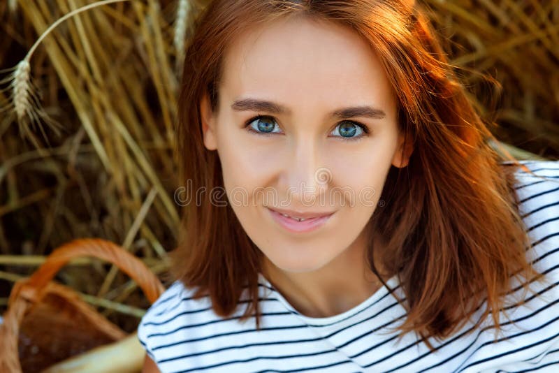 A pretty smiling young woman against the background of rye ears. Beautiful brunette on a wheat field at sunset. A lady in nature.