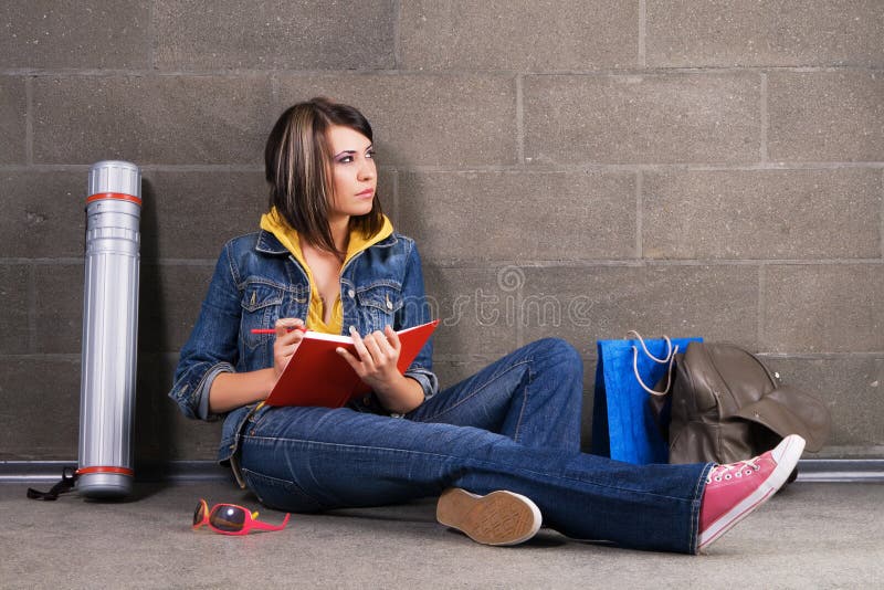 Pretty student near the wall writing at notebook