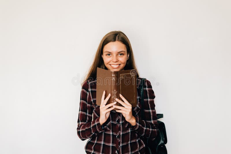 Pretty teenager girl student with book in her hands hiding face with copy space and white background smiling royalty free stock photography Pretty teenager girl student with book in her hands hiding face with copy space and white background smiling royalty free stock photography