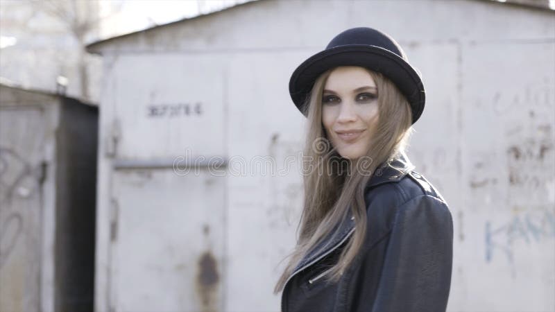 Pretty trendy girl with black stylish hat and leather jacket posing at old building in warm sunlight. Action. Smiling stock images Pretty trendy girl with black stylish hat and leather jacket posing at old building in warm sunlight. Action. Smiling stock images