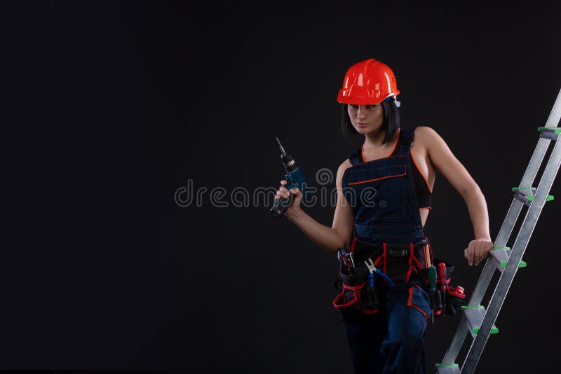 Pretty woman builder in helmet with drill in her hands standing on a ladder and looking away on black background royalty free stock photography Pretty woman builder in helmet with drill in her hands standing on a ladder and looking away on black background royalty free stock photography
