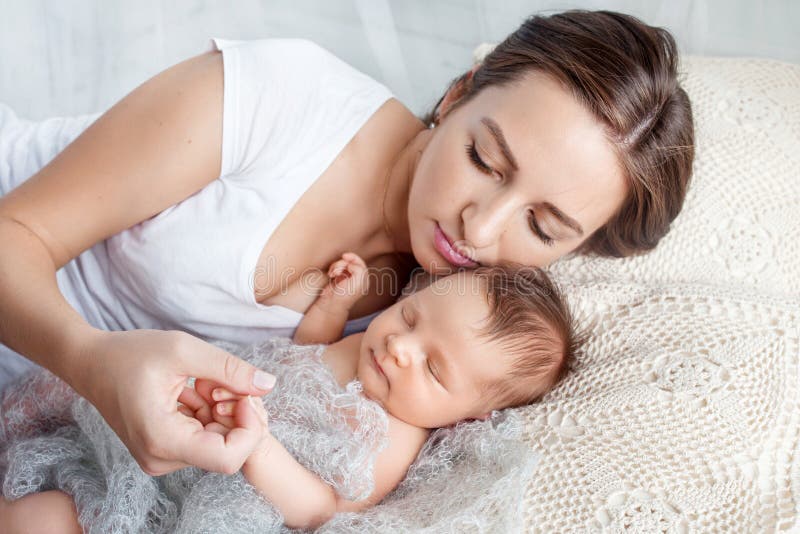 Pretty woman holding a newborn baby in her arms. Happy mother and her slipping newborn baby in the bed stock images Pretty woman holding a newborn baby in her arms. Happy mother and her slipping newborn baby in the bed stock images
