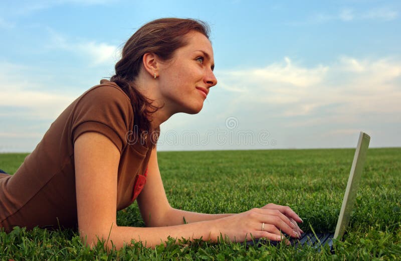 Pretty woman with laptop on the green grass