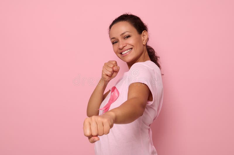 Pretty woman in pink t-shirt and cancer awareness ribbon stands in fighting stance to mark the fight against cancer, in honor of