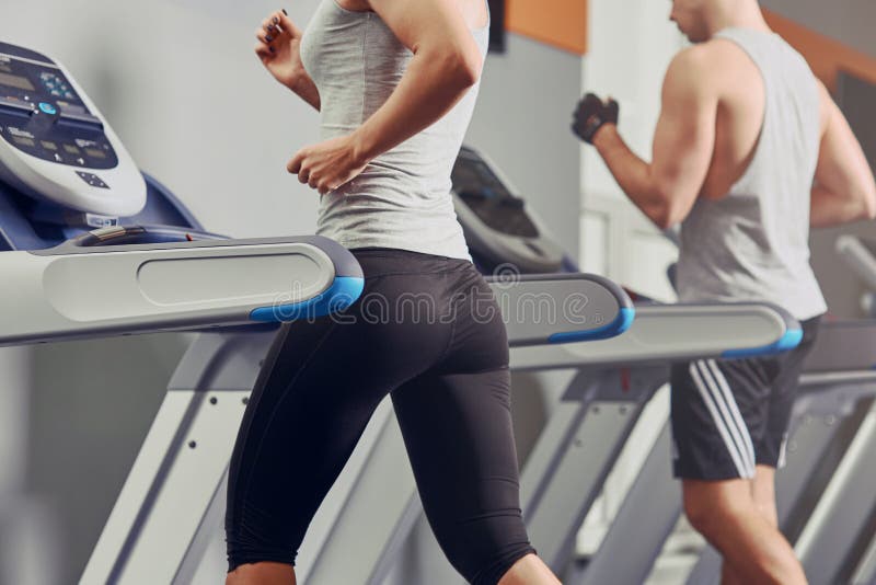 Pretty woman running on treadmill with fit young man on background