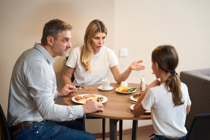 Family mother, father and dauter having breakfast in kitchen in hotel room