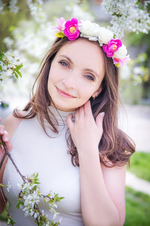 Pretty woman with wreath among apple blossom