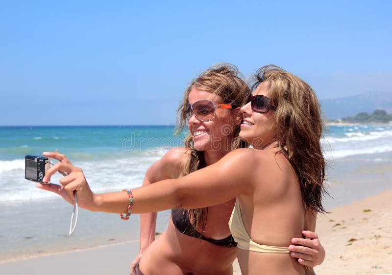 Zwei junge Frauen, die Fotos von jedem anderen auf einem sonnigen Strand.