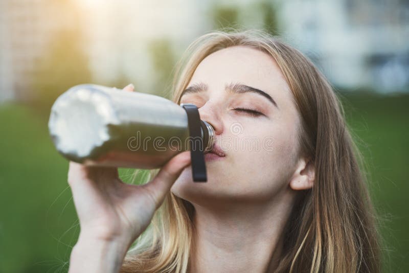 Pretty young blonde woman drinking water from stainless steel bottle