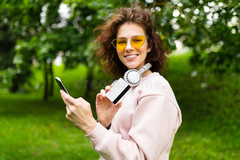 Pretty young caucasian woman is engaged in freelance in the park with credit card