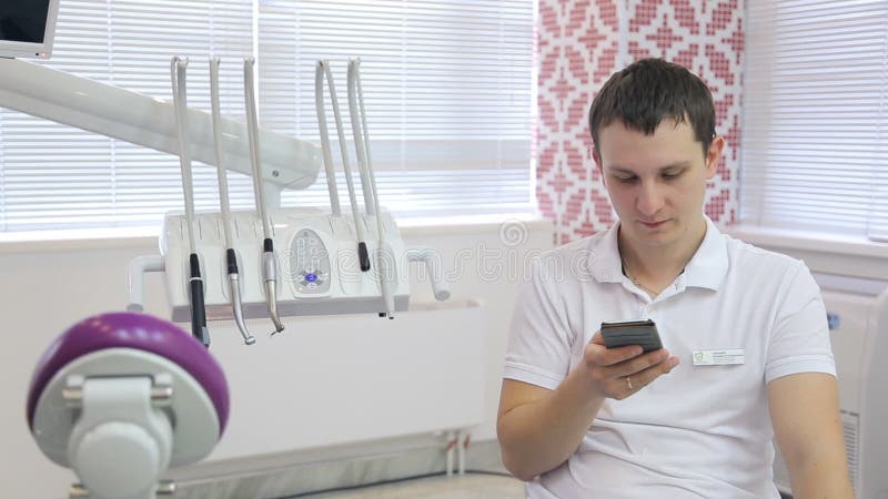 Pretty young doctor sits on chair in cabinet and chats on telephone.