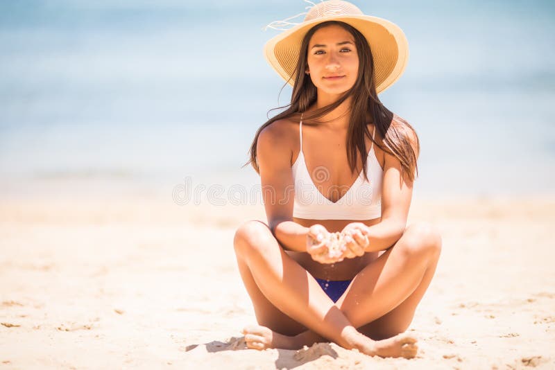 Pretty young latin pretty girl at beach. Woman sitting on sands have active time in summer playing with sand. Summertime carefree
