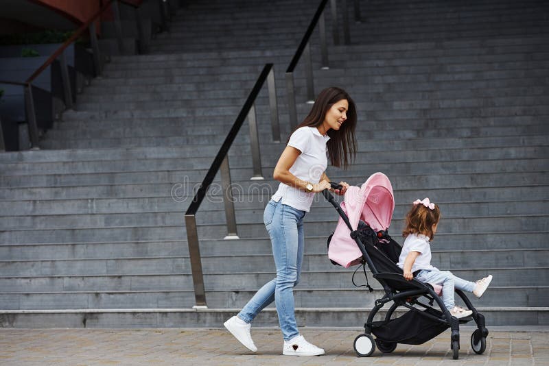 Pretty young mother and her little daughter in pink pram have walk in the city 库存图片 Pretty young mother and her little daughter in pink pram have walk in the city 库存图片