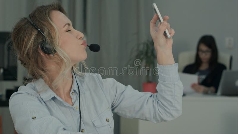 Pretty young office worker in headset taking funny selfies at workplace