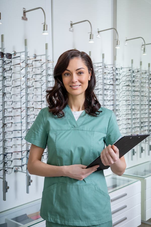 Pretty young ophthalmologist in a lab coat standing the the stand with glasses royalty free stock photos