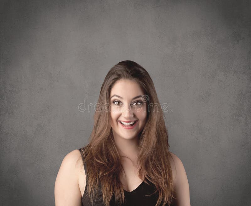 A pretty young teenage girl standing in front of a grey clear empty urban wall background concept while making funny faces. A pretty young teenage girl standing in front of a grey clear empty urban wall background concept while making funny faces.