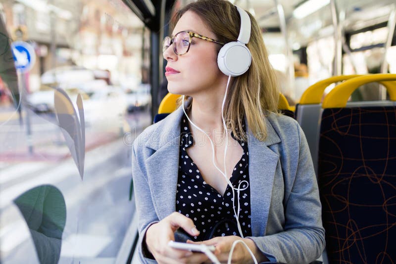 Pretty young woman listening to music with mobile phone at the bus.