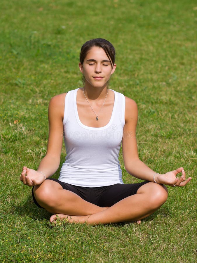 Pretty young woman meditating on grass