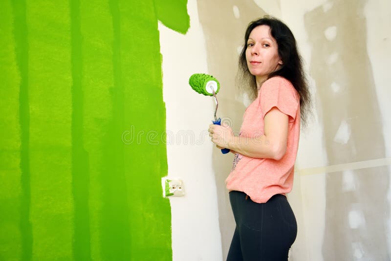 Pretty young woman in pink t-shirt is smiling and keeping roller, painting green interior wall in a new home royalty free stock photos Pretty young woman in pink t-shirt is smiling and keeping roller, painting green interior wall in a new home royalty free stock photos