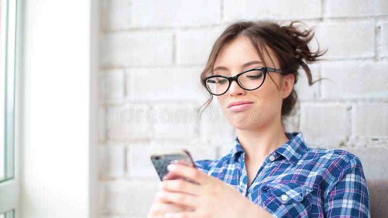 Pretty young woman using smartphone smiling happy indoors. Girl sms texting using app on smart phone at home.