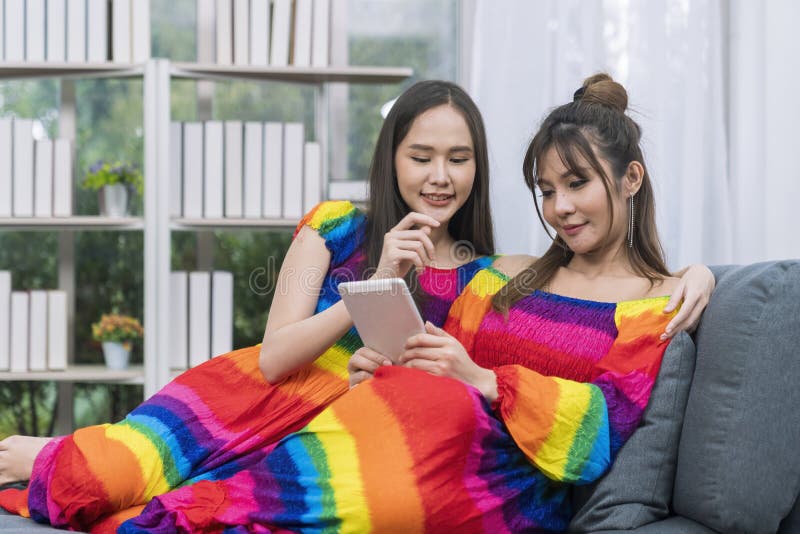 Pride Month. Young woman with tablet sitting on sofa in living room. Young couple shopping online on the sofa in their living room royalty free stock photos