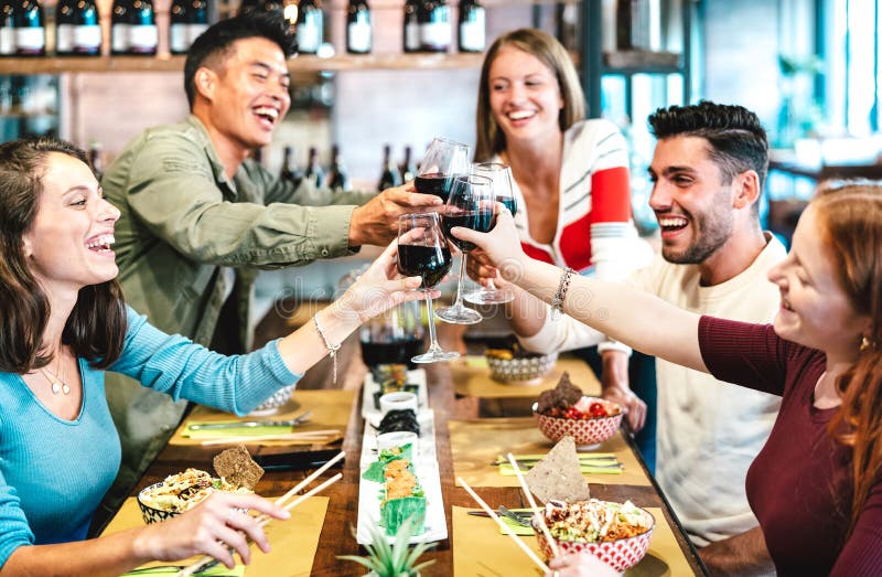 Prieteni multirasiști care toastează vinul roșu la restaurantul sushi, conceptul de stil de viață al băuturilor și al produselor a stock photos